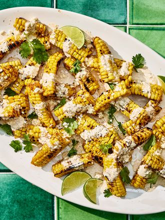 Bright colorful photo of grilled corn, topped with sauce, cheese cilantro and limes. 